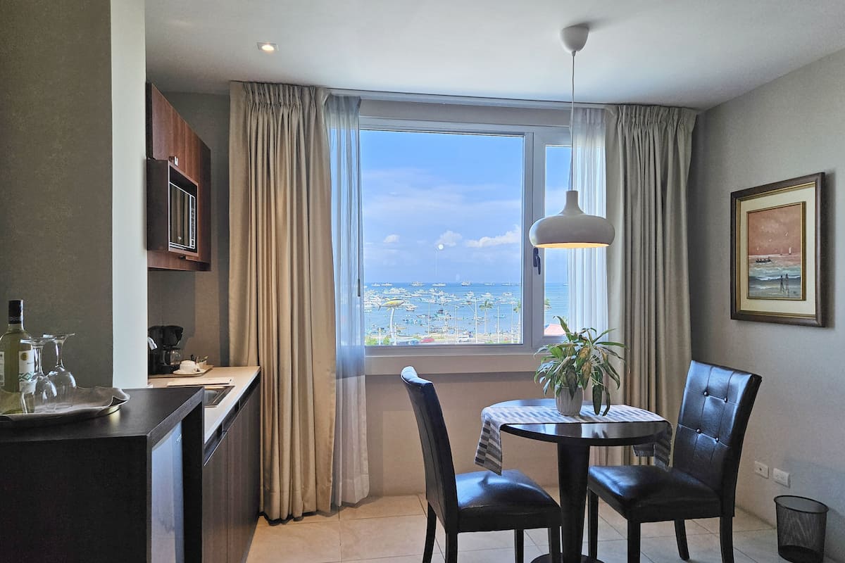 A dining area with a view of the sea, a table with chairs, a potted plant, and a framed picture on the wall.