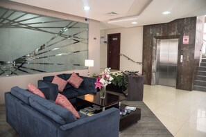 A modern lobby with a blue sofa, a coffee table, a vase of flowers, a staircase, and an elevator. - Hotel Perla Spondylus (Manta)