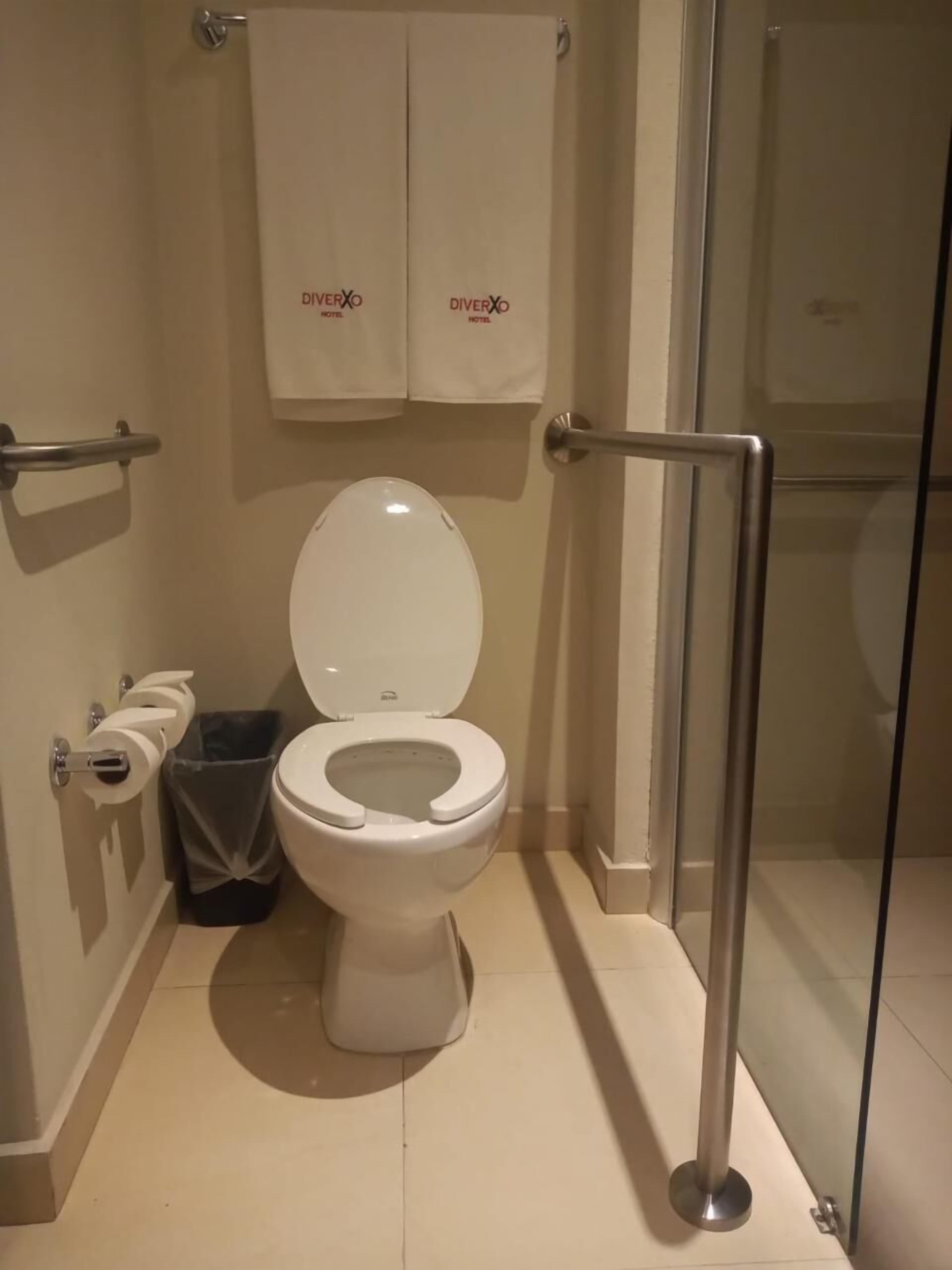 A modern bathroom with a white toilet, a glass shower enclosure, and a towel rack with 'DiverXO Hotel' branding.