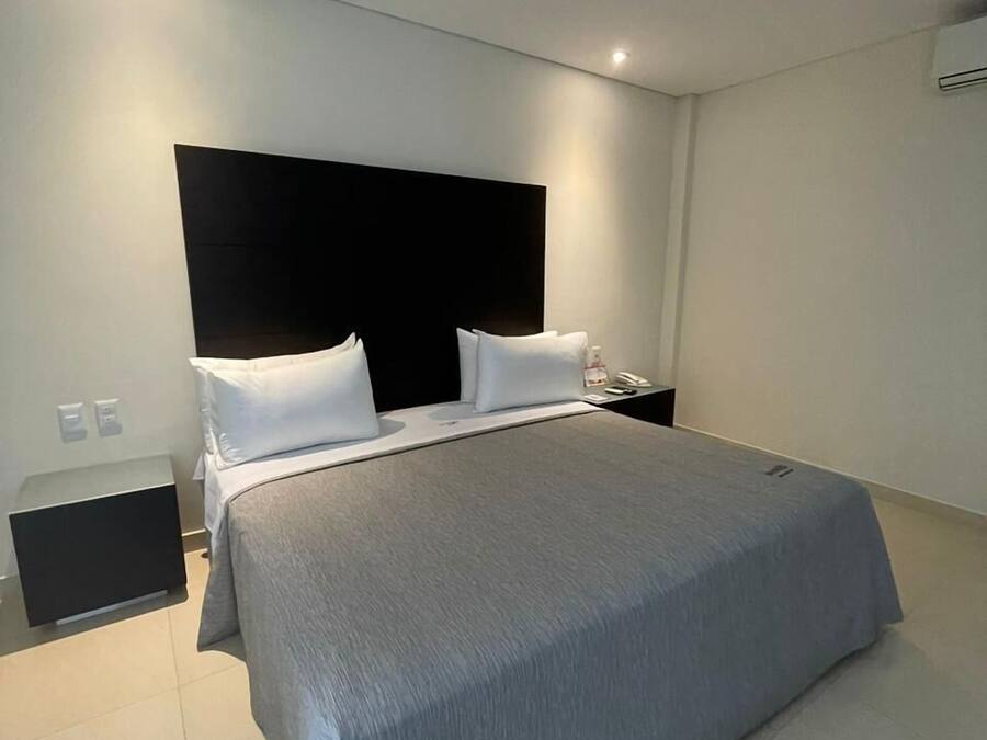 A modern bedroom with a large bed, a black headboard, white pillows, and a bedside table with a lamp.