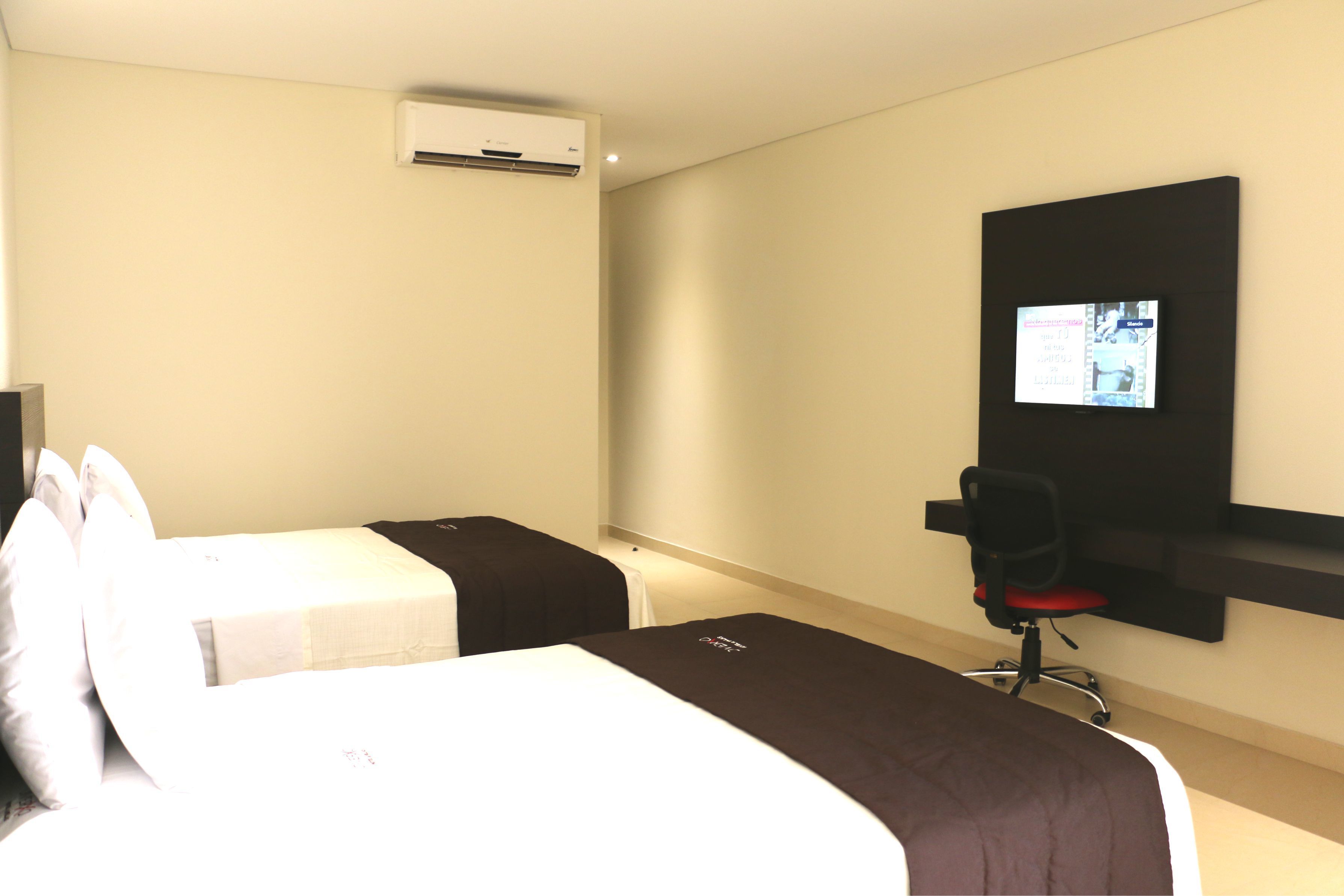 Habitación de hotel con dos camas, un televisor en la pared y un escritorio con una silla.