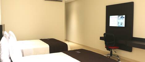 Habitación de hotel con dos camas, un televisor en la pared y un escritorio con una silla.