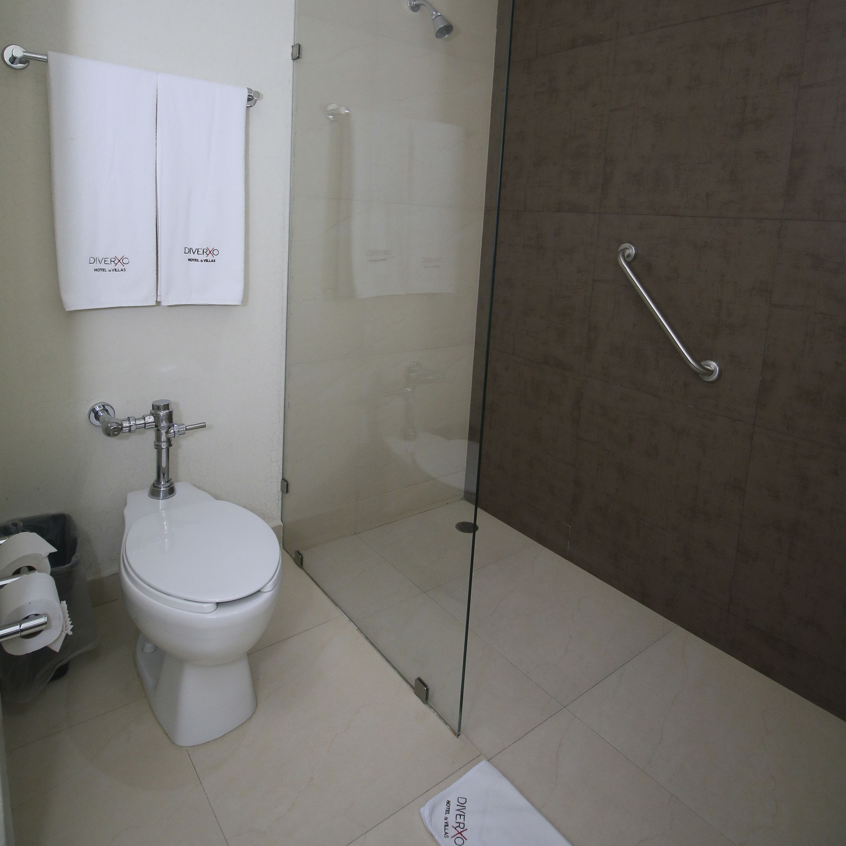 A bathroom with a toilet, a glass shower enclosure, and two white towels hanging on a rack.