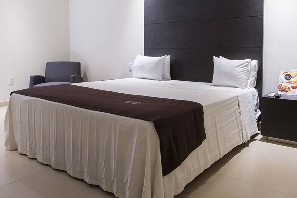 Una habitación de hotel moderna con una cama grande, un cabecero oscuro y un escritorio pequeño con un control remoto.