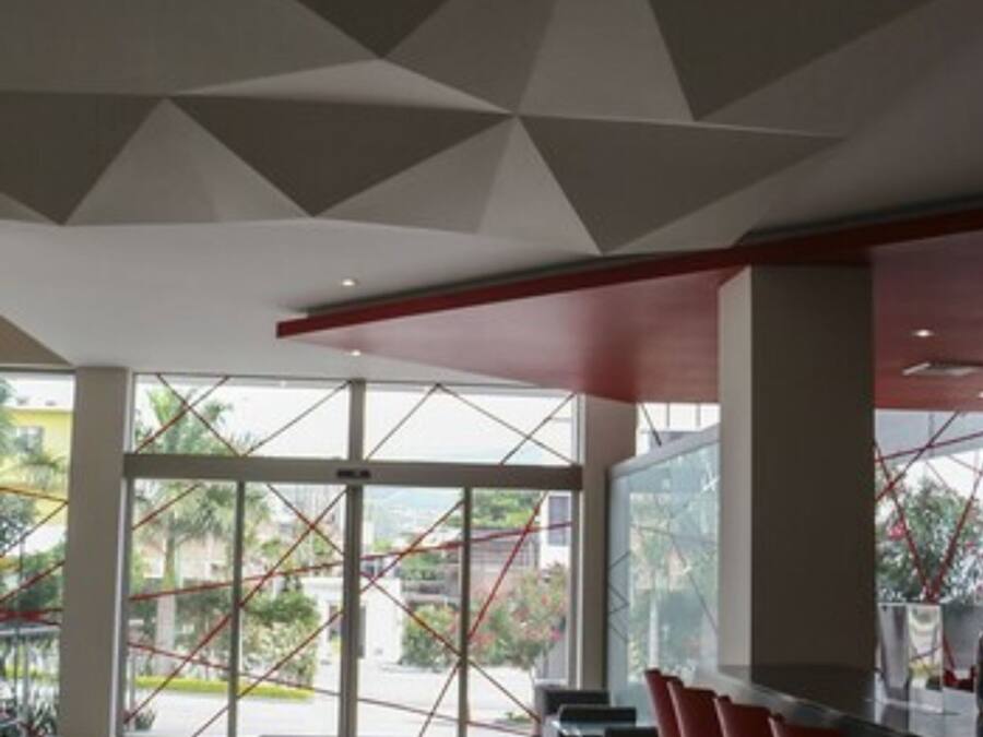 Un interior moderno con diseño geométrico en el techo, ventanas amplias y taburetes rojos.
