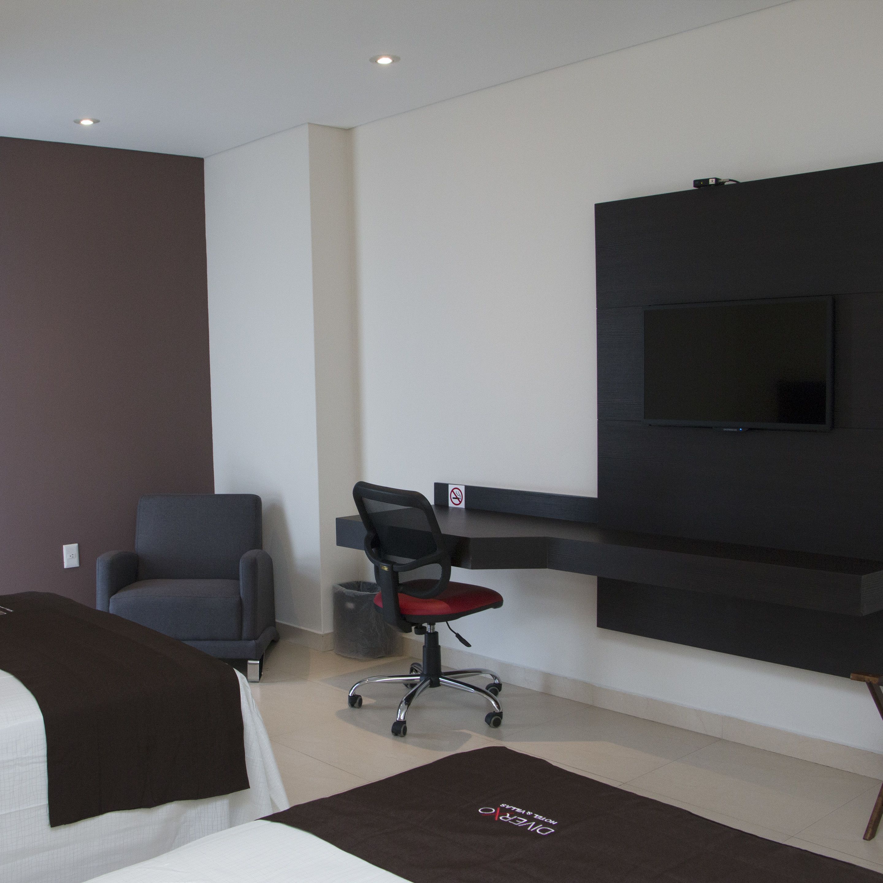 A modern hotel room with a bed, a desk, a chair, and a TV mounted on the wall.
