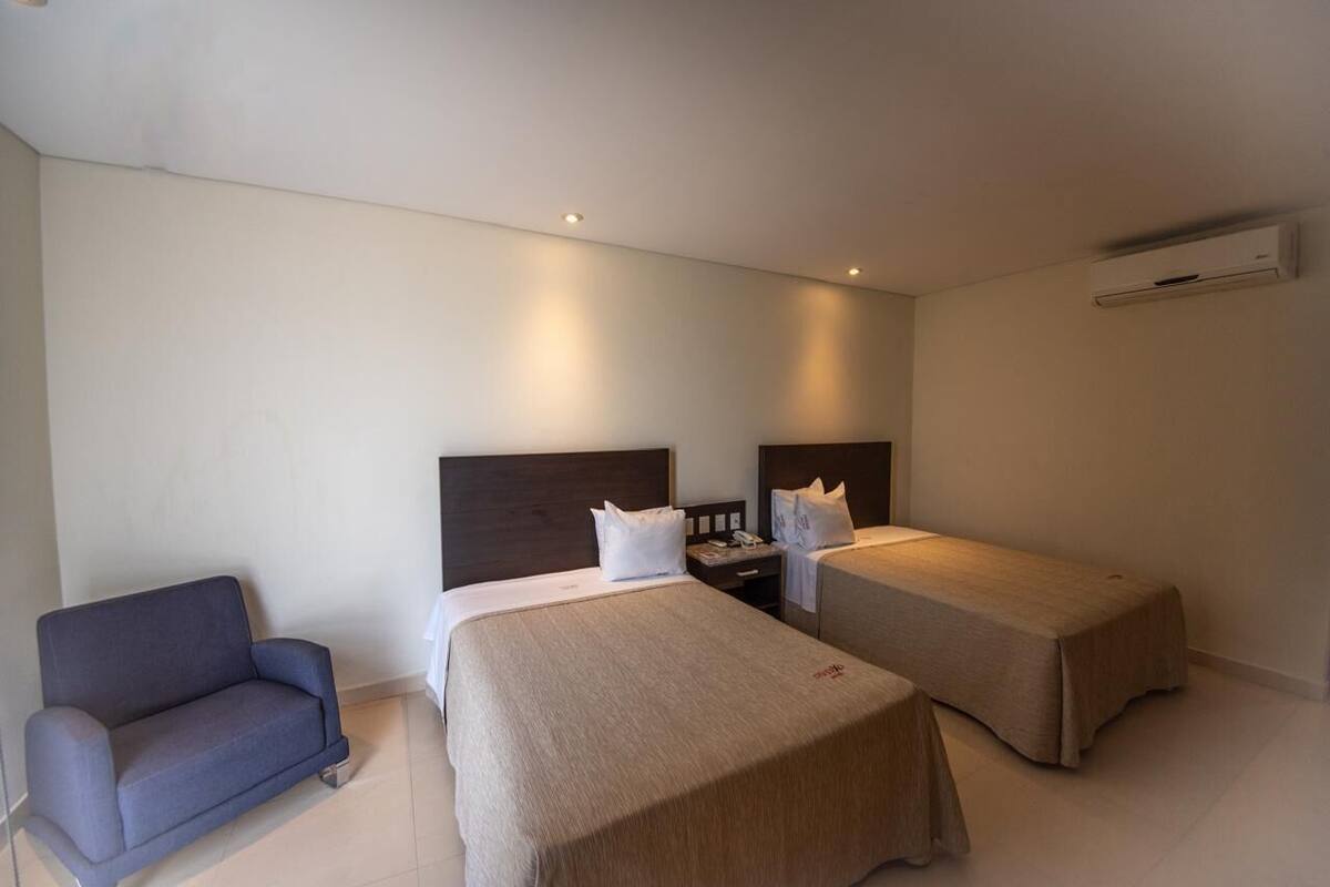 Una habitación de hotel con dos camas individuales, un sofá, una mesita de noche y un equipo de aire acondicionado.