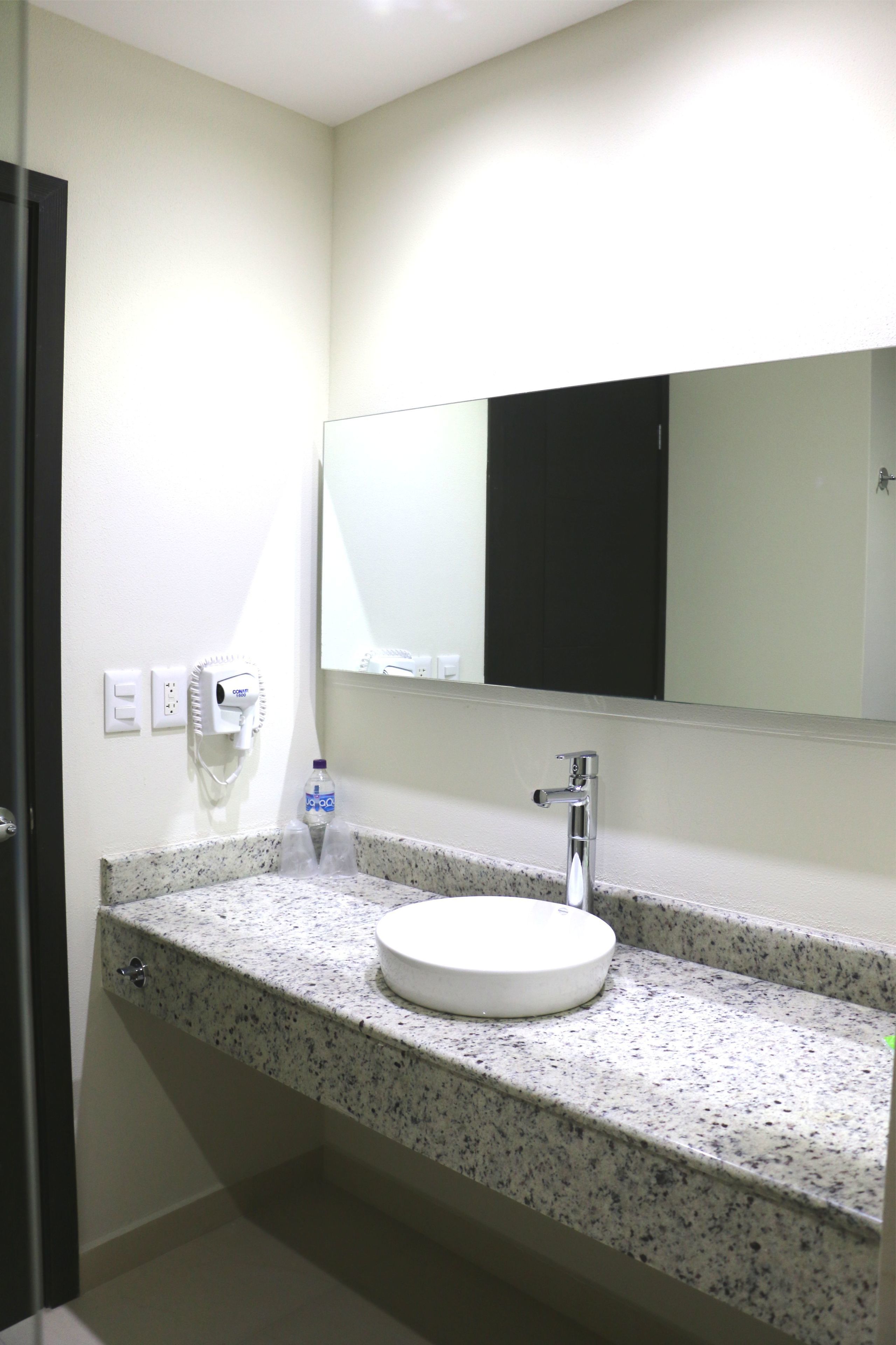 Un baño con encimera de granito, lavabo blanco, espejo y mueble negro.