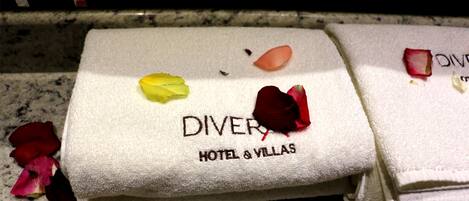 A folded towel with "DIVER HOTEL & VILLAS" printed on it, placed on a marble surface with scattered rose petals.