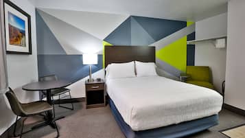 A hotel room with a bed, a desk, a chair, a nightstand, and a lamp.