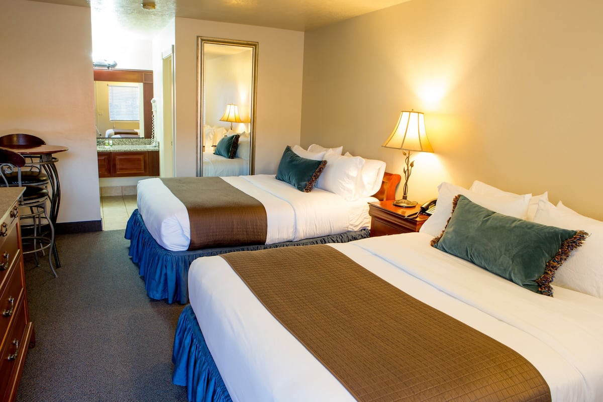 A hotel room with two beds, a desk, and a mirror.