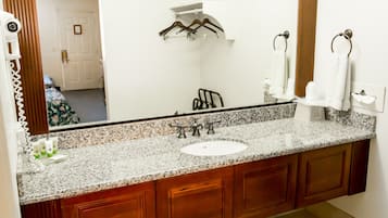 A bathroom with a granite countertop, a sink, wooden cabinets, a large mirror, and a towel rack.