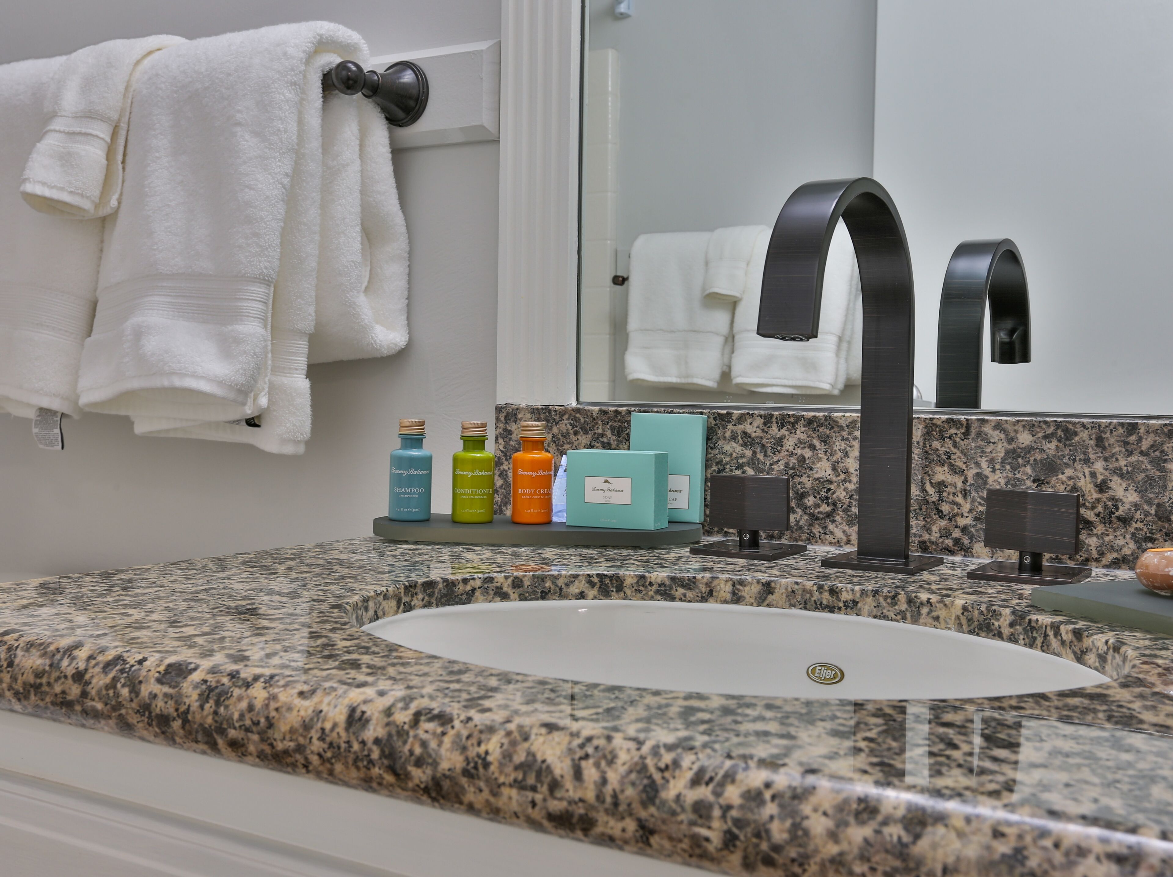 Ein Badezimmer mit Granitplatte, einem weißen Waschbecken, einem schwarzen Wasserhahn und Pflegeprodukten auf einem Regal.