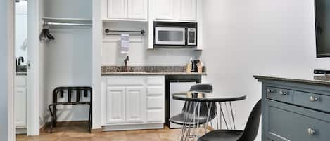A compact kitchen with white cabinets, a granite countertop, a microwave, a small dining table with chairs, and a gray dresser.
