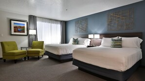 Una habitación de hotel con dos camas, un sillón verde, una mesita y un cuadro en la pared.