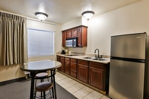 Cocina compacta con armarios de madera, un refrigerador de acero inoxidable, un microondas y una pequeña mesa de comedor con dos taburetes.