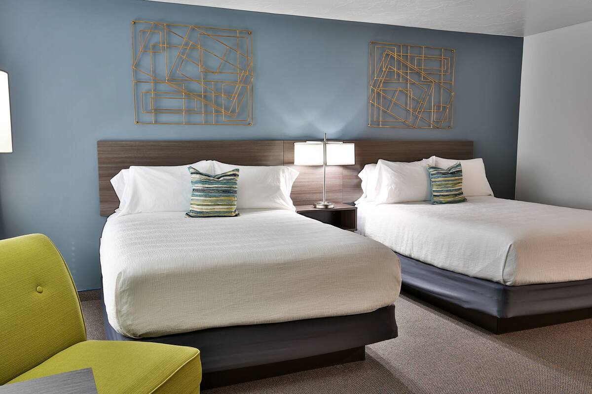 A hotel room with two beds, a nightstand with a lamp, and a bright yellow chair.