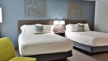 A hotel room with two beds, a nightstand with a lamp, and a bright yellow chair.