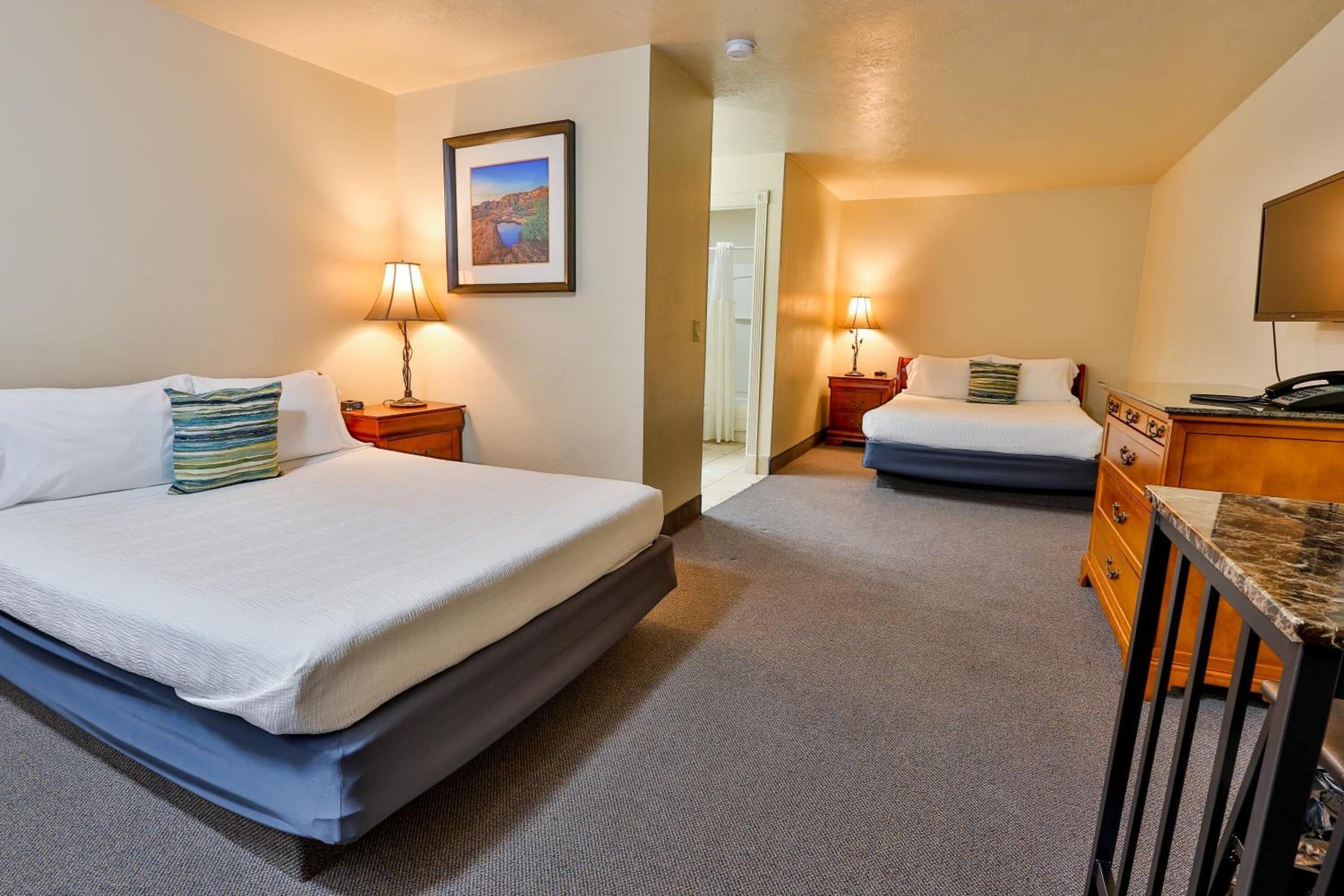 A hotel room with two beds, a desk, and a television.