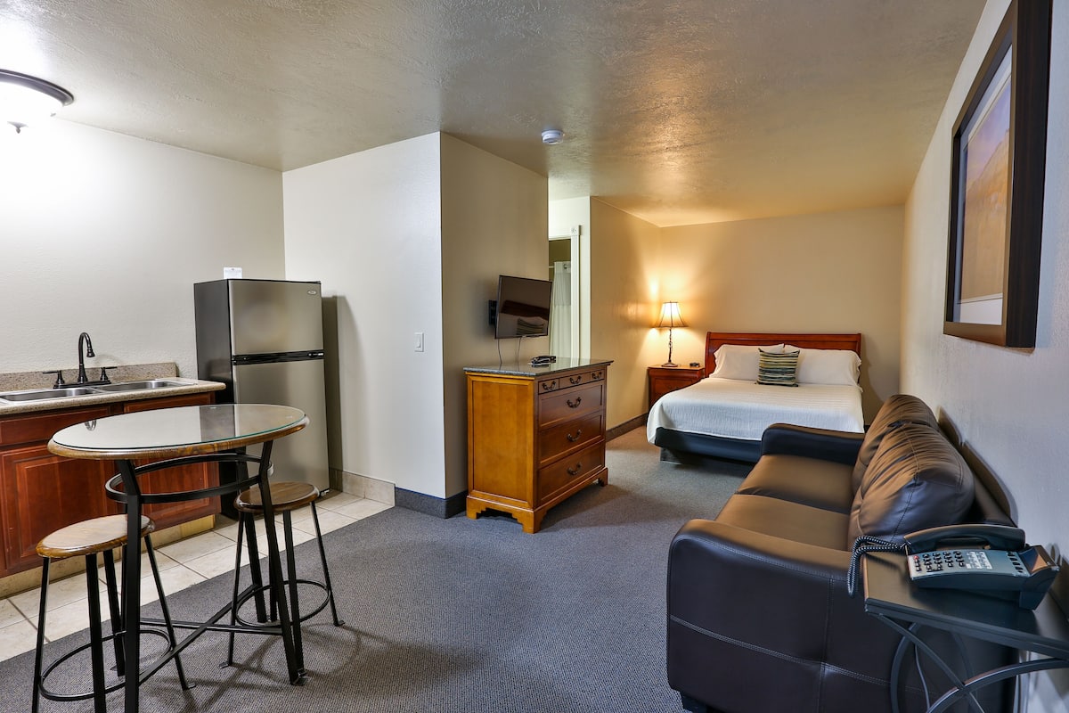A compact hotel room with a kitchenette, a bed, a sofa, and a small table.
