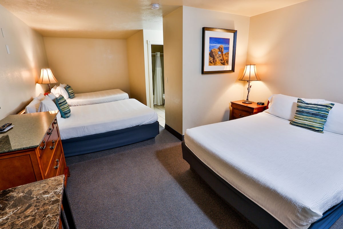A hotel room with two beds, a desk, and a bathroom visible through an open door.