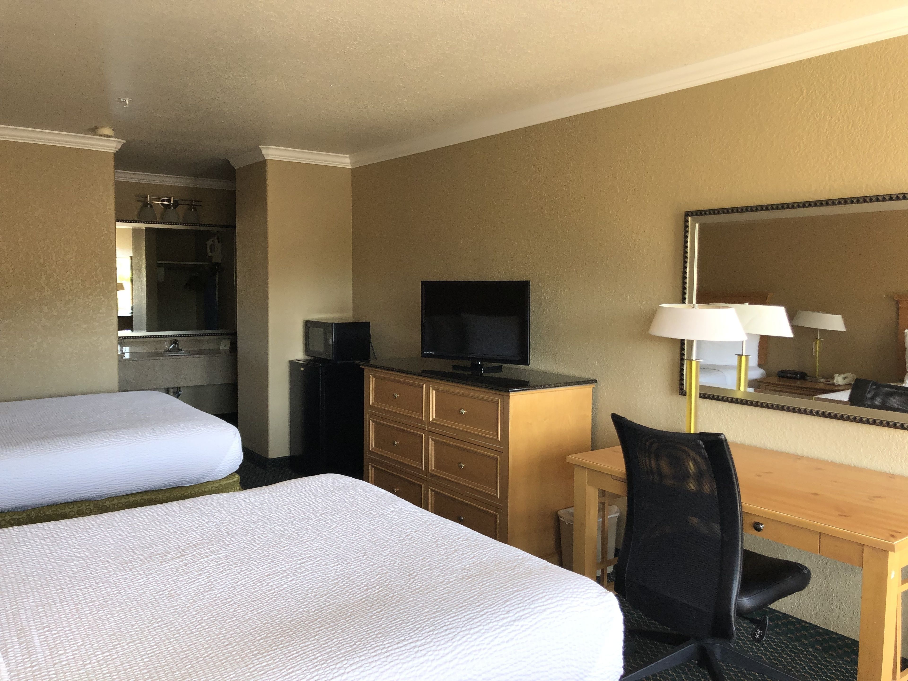 Une chambre d’hôtel avec deux lits, un bureau avec une chaise, une télévision, une commode et un miroir.