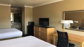 Une chambre d’hôtel avec deux lits, un bureau avec une chaise, une télévision, une commode et un miroir.