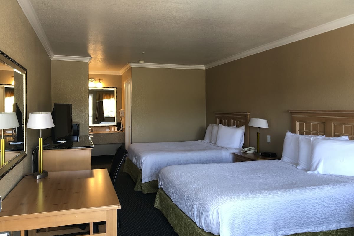 A hotel room with two beds, a desk, a mirror, and a nightstand with a lamp.