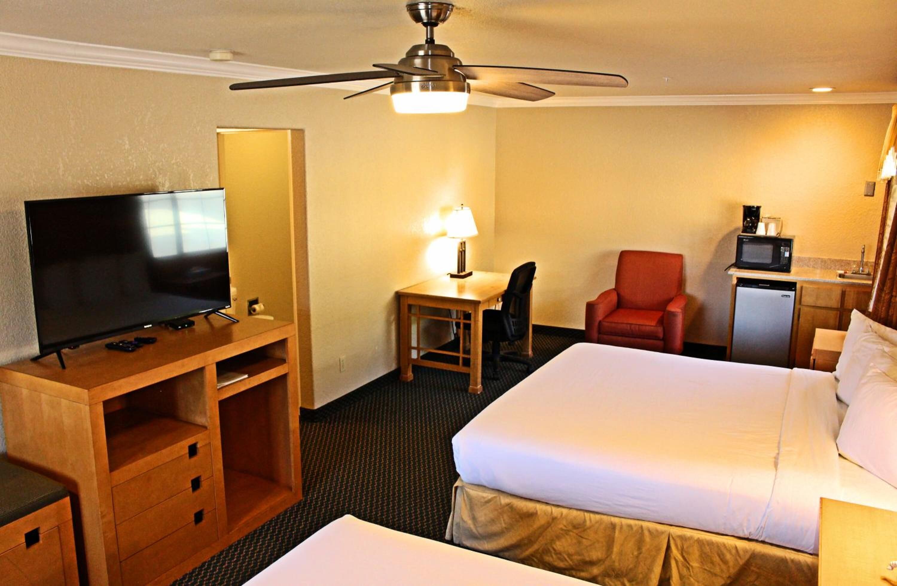 Une chambre d’hôtel équipée d’un lit, d’un bureau avec une télévision, d’une chaise, d’un four à micro-ondes et d’un ventilateur de plafond.
