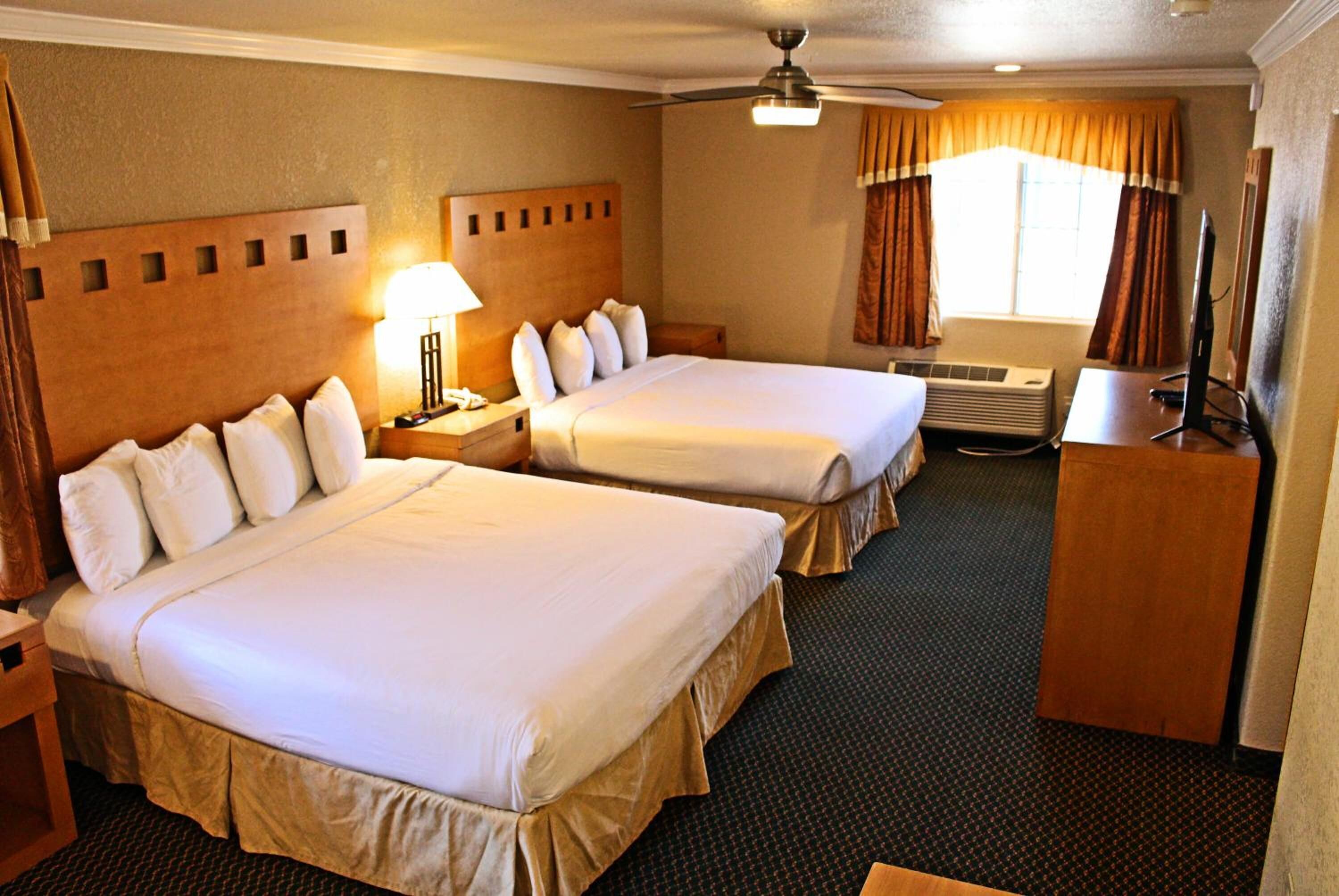A hotel room with two beds, a desk, a chair, a lamp, an air conditioning unit, and a ceiling fan.