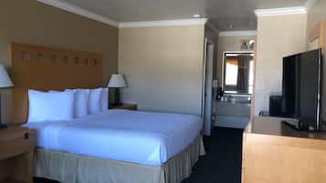 Habitación de hotel con una cama grande, un escritorio con lámpara, televisión y baño visible a través de una puerta abierta.