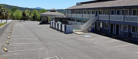A motel with a parking lot, a covered area, and a staircase leading to the building.