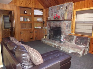 A cozy living room with a leather sofa, wooden shelves, a stone fireplace, and a clock.