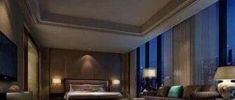 Habitación de hotel con una cama grande, una zona de estar con sofá y sillones, una mesa de centro y un amplio ventanal con vistas.