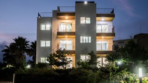 Un immeuble résidentiel à plusieurs étages, doté de balcons, de grandes fenêtres et d’une façade bien éclairée au crépuscule.
