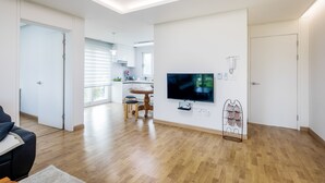 Un salon moderne doté d’un téléviseur à écran plat, de planchers en bois, d’un coin repas avec une table et des chaises, et d’une cuisine en arrière-plan.