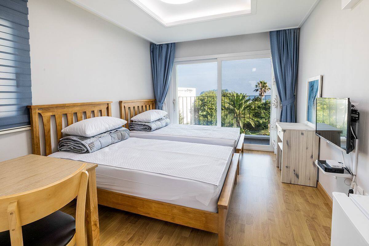 Une chambre avec deux lits, un bureau en bois, une télévision et un balcon avec vue.