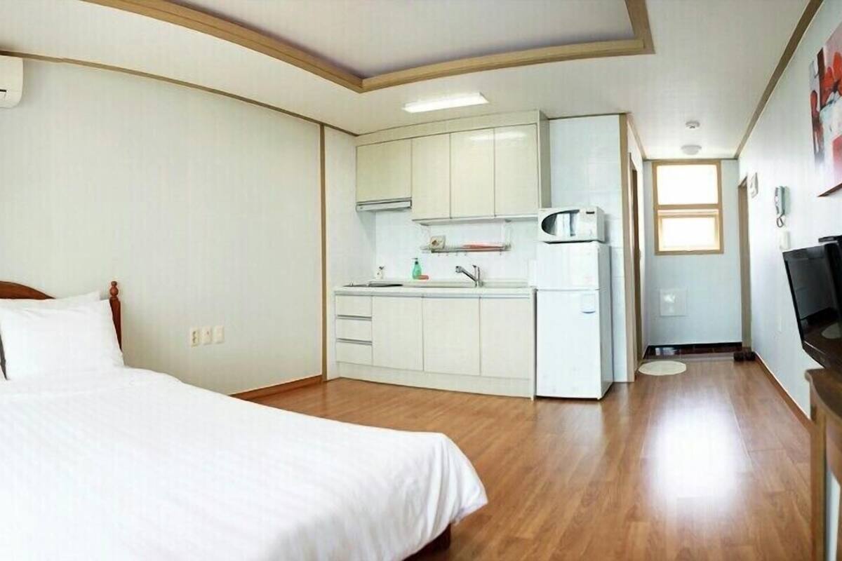 Une chambre d’hôtel avec un lit, une kitchenette et un téléviseur posé sur un meuble en bois.