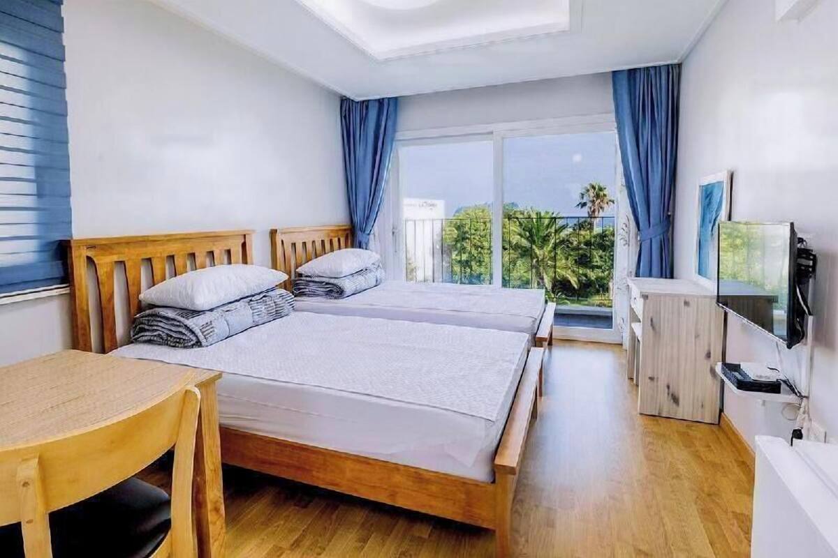Une chambre avec deux lits, une table en bois, une télévision et un balcon avec vue.