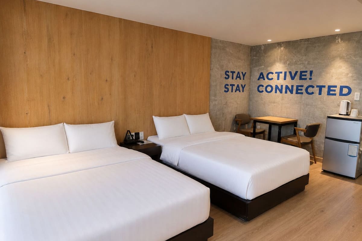 Een hotelkamer met twee bedden, een tafeltje, stoelen, een koelkast en inspirerende decoratie aan de muur.