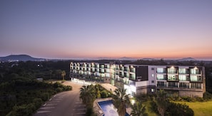 A modern hotel with multiple floors, a swimming pool, and a parking lot.