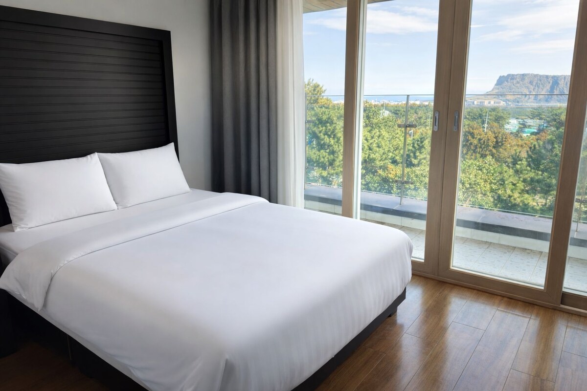 Une chambre d’hôtel moderne avec un grand lit, une tête de lit sombre et une vue sur un paysage montagneux grâce à de grandes fenêtres du sol au plafond.