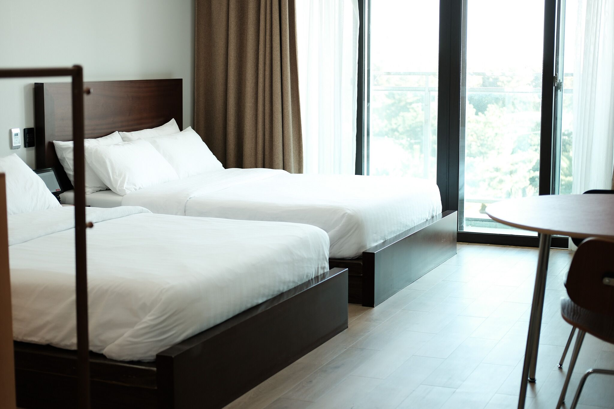 A hotel room with two beds, a dining area, and large windows.