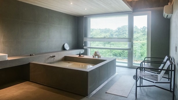 Une salle de bain moderne avec une grande baignoire, une fenêtre avec des stores et un banc.