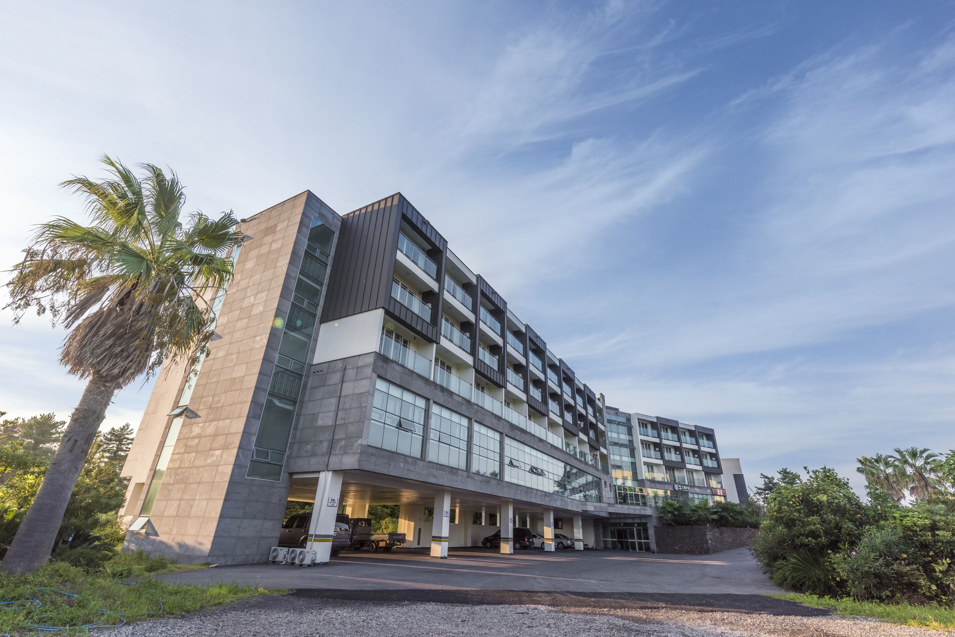 A modern multi-story hotel with a central atrium, large windows, and a parking area.