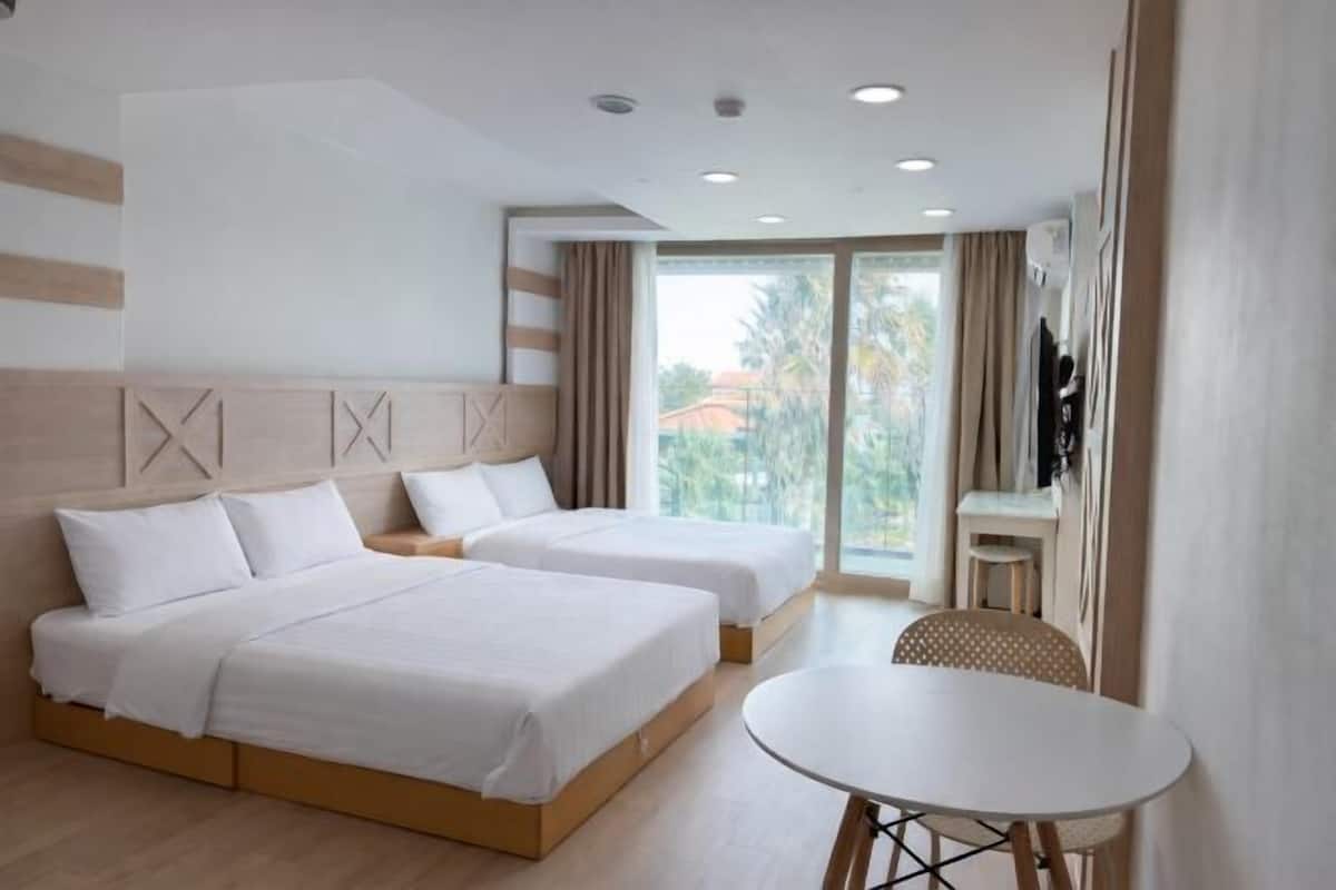 Een hotelkamer met twee bedden, een ronde tafel en een balkon met gordijnen.