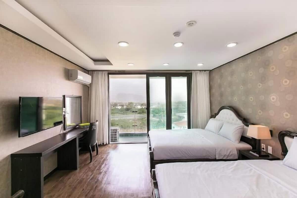Hotelkamer met televisie, bureau, twee bedden en een groot raam met uitzicht.