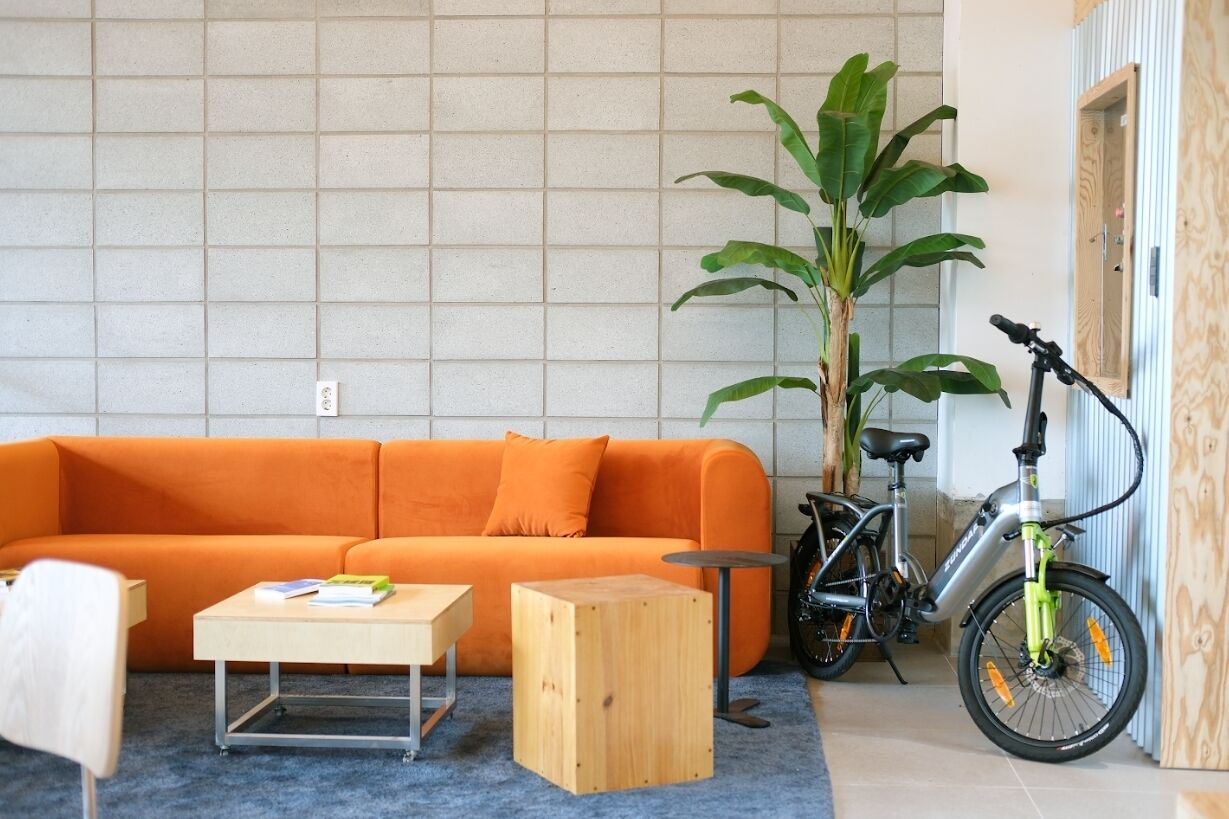A modern living room with an orange sofa, a wooden coffee table, a small side table, and a bicycle.