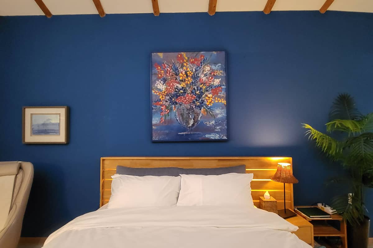 Une chambre à coucher avec un lit, une table de chevet avec une lampe, une chaise et un tableau au mur.