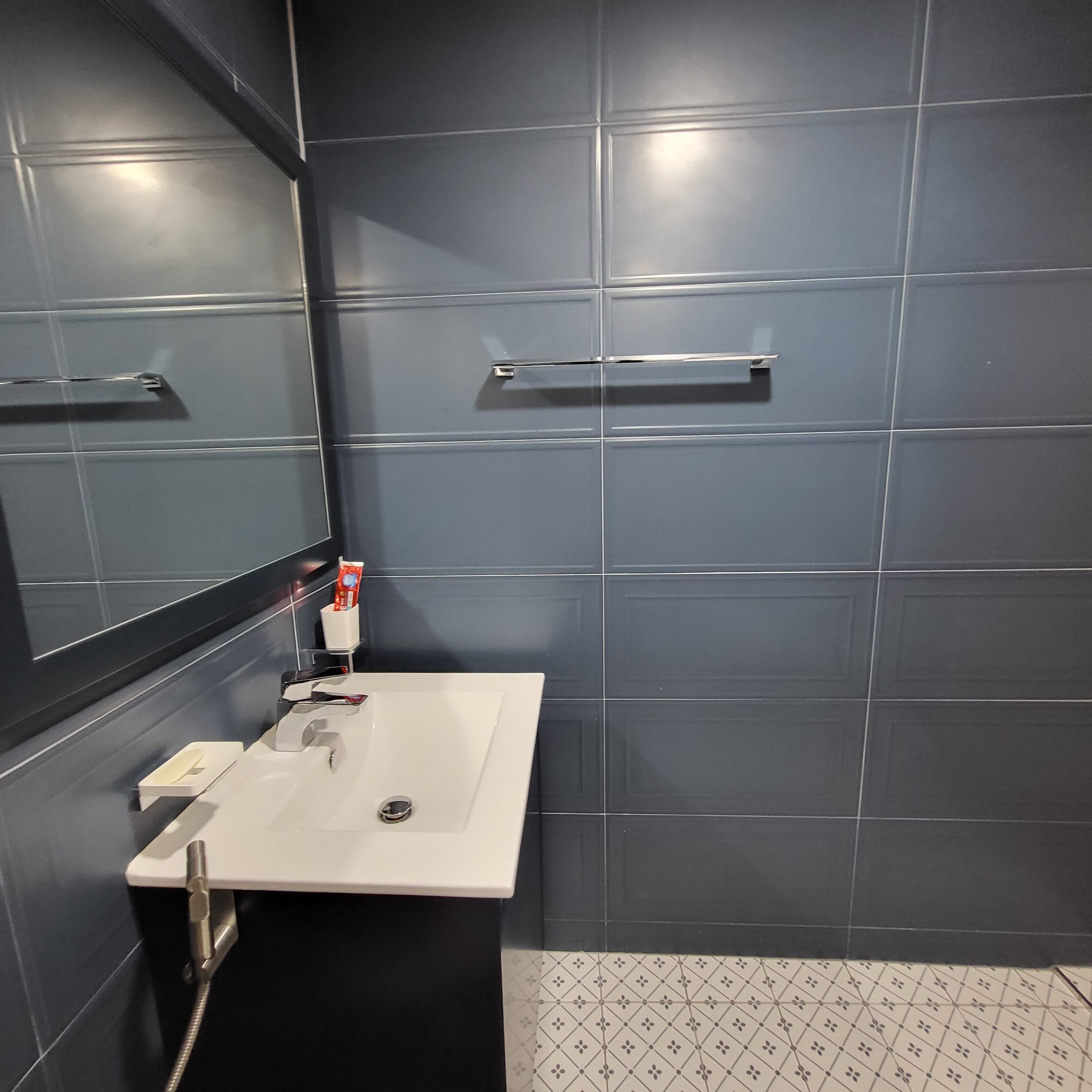 A bathroom with a white sink, dark blue tiles, a mirror, and a shower area.